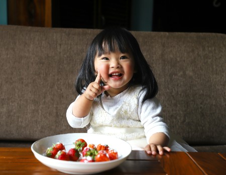 Smiling child with dark black hair, eating bright red strawberries